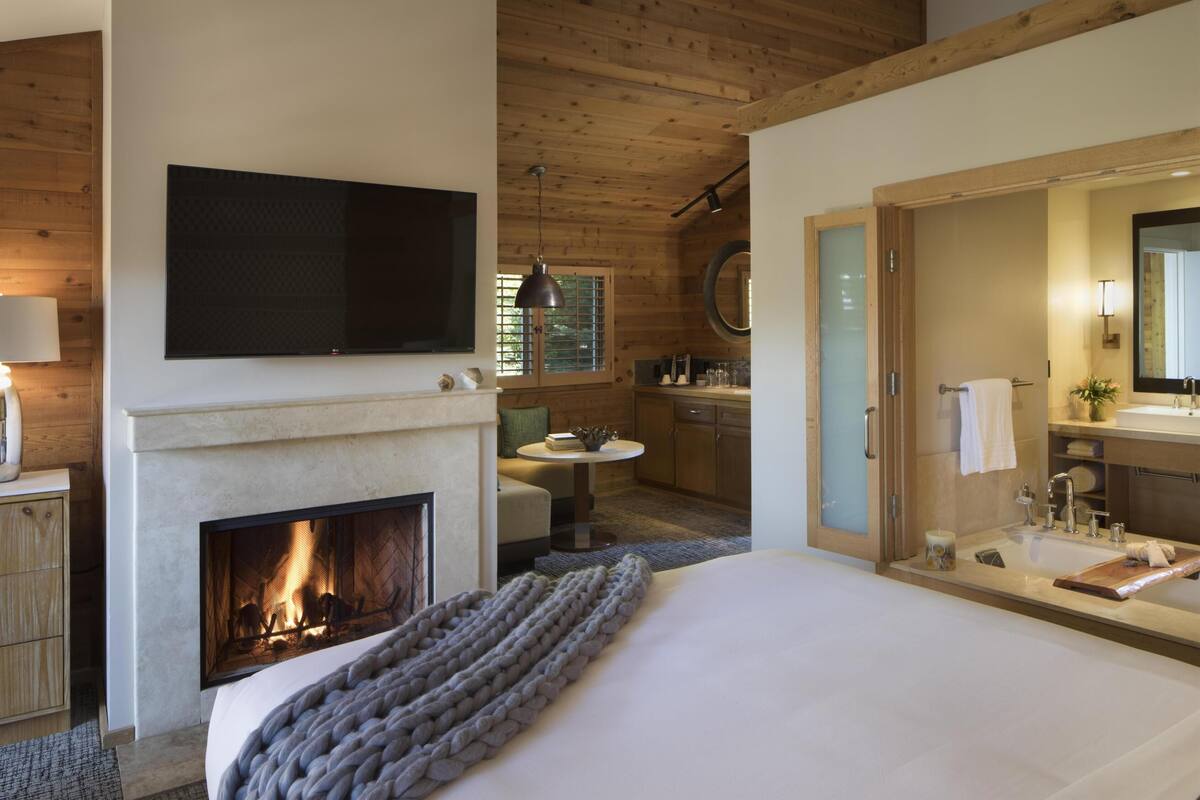 Un dormitorio con chimenea, una cama, un televisor, un baño con espejo y un comedor con mesa y sillas.