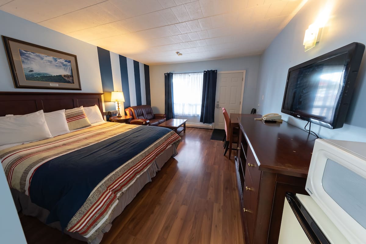 A hotel room with a large bed, a desk with a television, a chair, a lamp, and a framed picture on the wall.