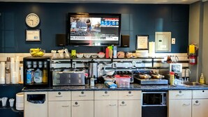 A modern kitchen with a flat-screen TV mounted above the counter, various kitchen appliances, and storage cabinets. - Villager Lodge (Niagara Falls)