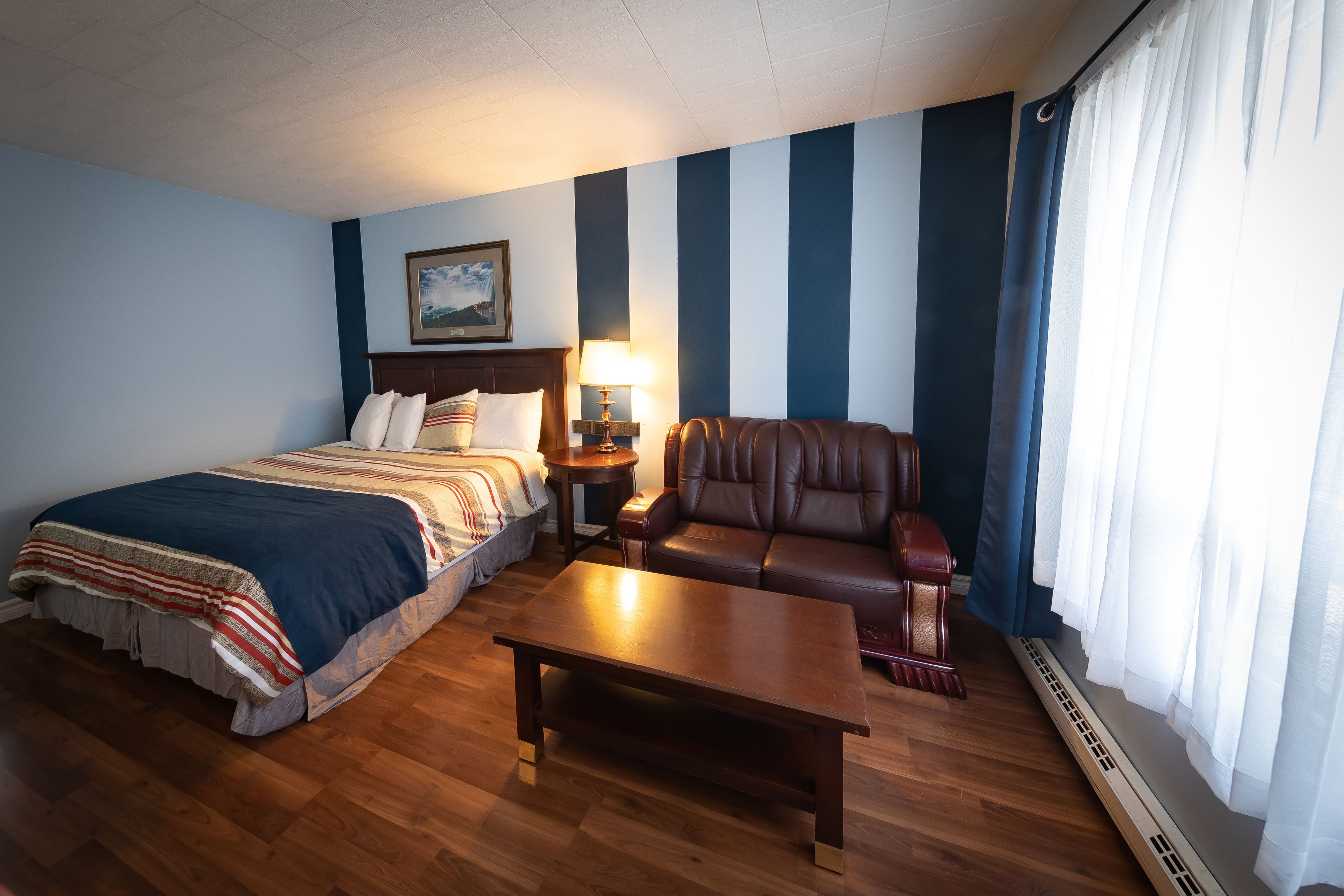 Une chambre d’hôtel comprenant un lit, un canapé, une table basse, une table de chevet, une lampe et une fenêtre avec des rideaux.