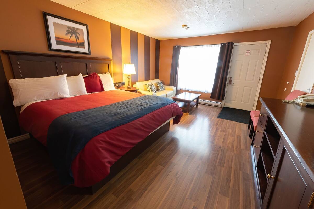 A hotel room with a large bed, a desk, a chair, a lamp, and a door.