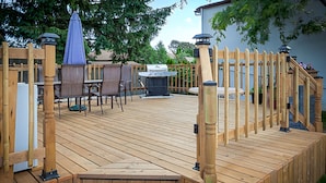 A wooden deck with a grill, chairs, and a table. - Villager Lodge (Niagara Falls)