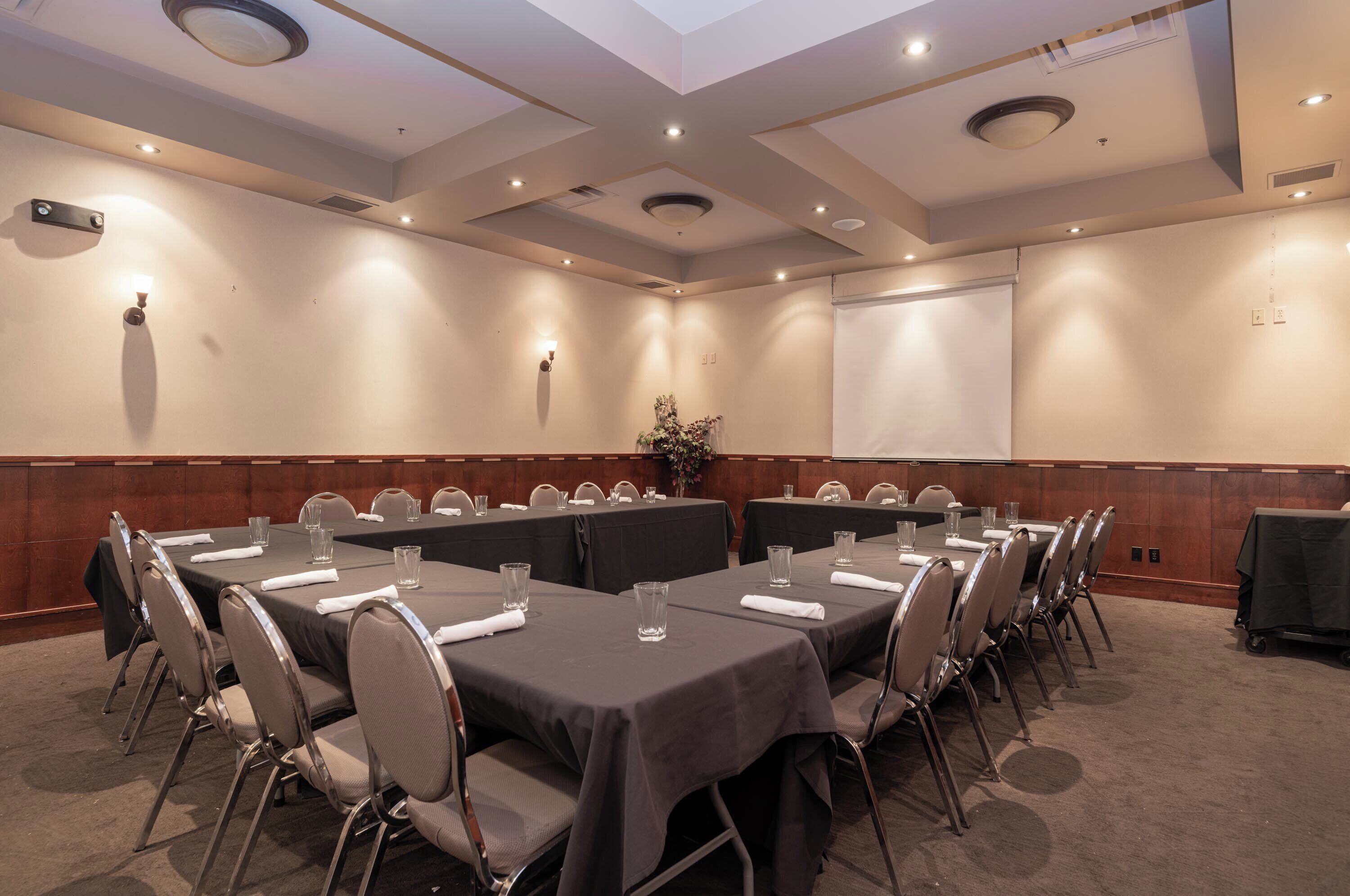 A conference room with long tables, chairs, and a projector screen.