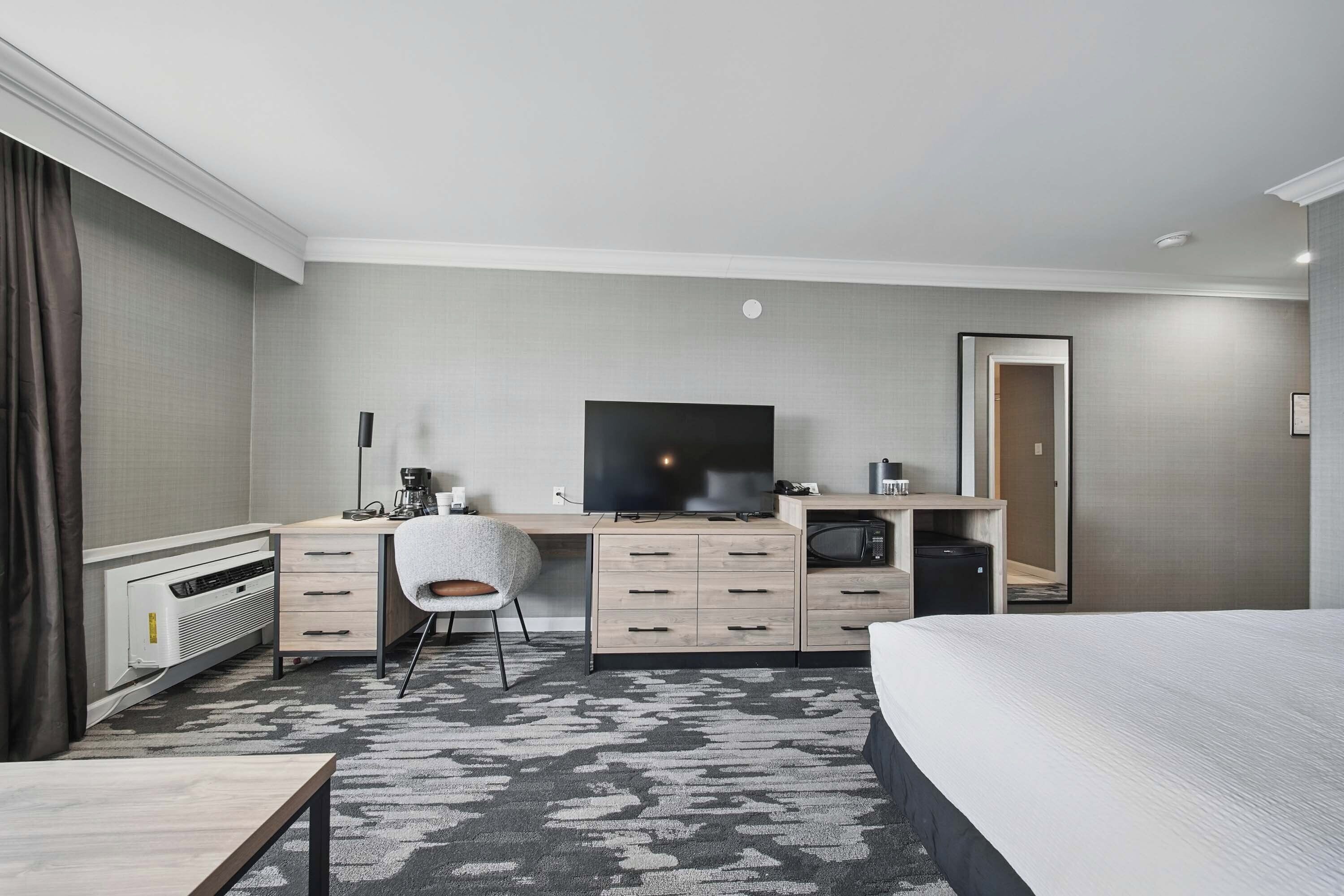 Habitación de hotel con cama, escritorio con televisor de pantalla plana, silla, cafetera, microondas y refrigerador pequeño.