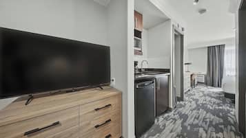 Habitación de hotel moderna con una televisión de pantalla plana sobre un aparador de madera, una zona de cocina con microondas y una alfombra estampada.