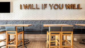 A modern interior with a brick wall, a motivational sign, wooden tables, and black leather chairs.