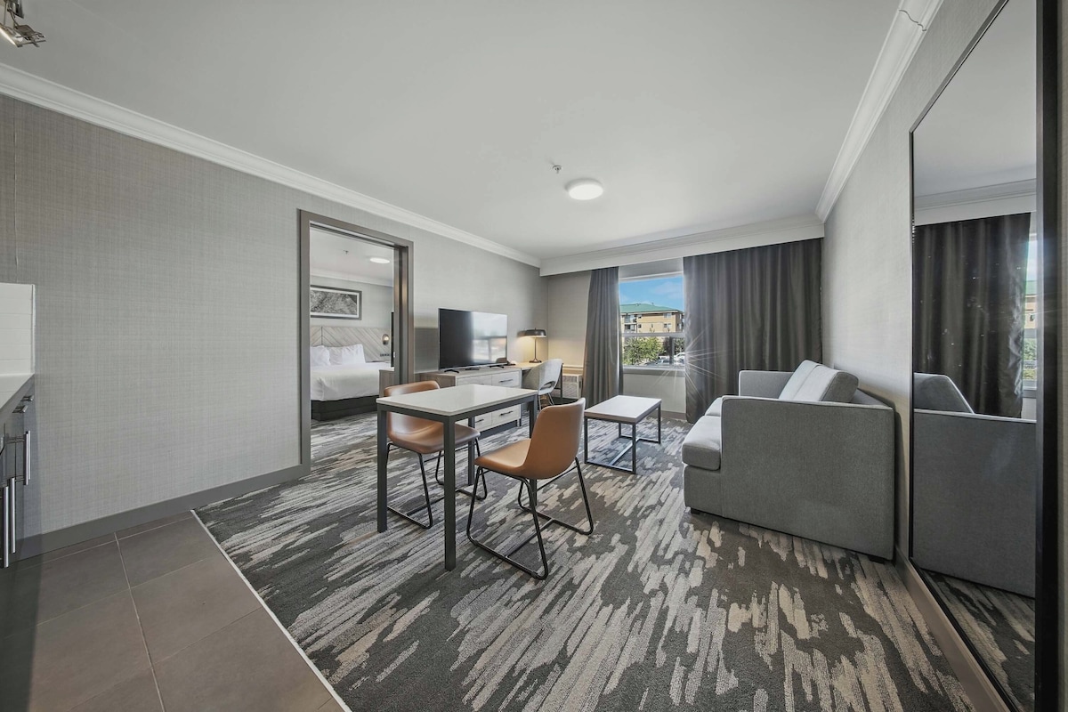 A hotel room with a bed, a desk, a chair, a sofa, and a view of the city.