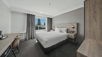 Een moderne hotelkamer met een groot bed, een bureau en uitzicht op bomen door een raam.