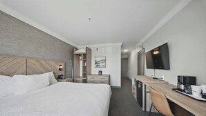 A hotel room with a large bed, a desk with a chair, a flat-screen TV, and a coffee maker.