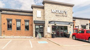 A brick building with a sign for "Moxie's Grill & Bar" and a red vehicle parked outside.