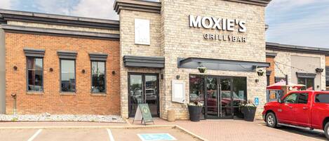 A brick building with a sign for "Moxie's Grill & Bar" and a red vehicle parked outside.