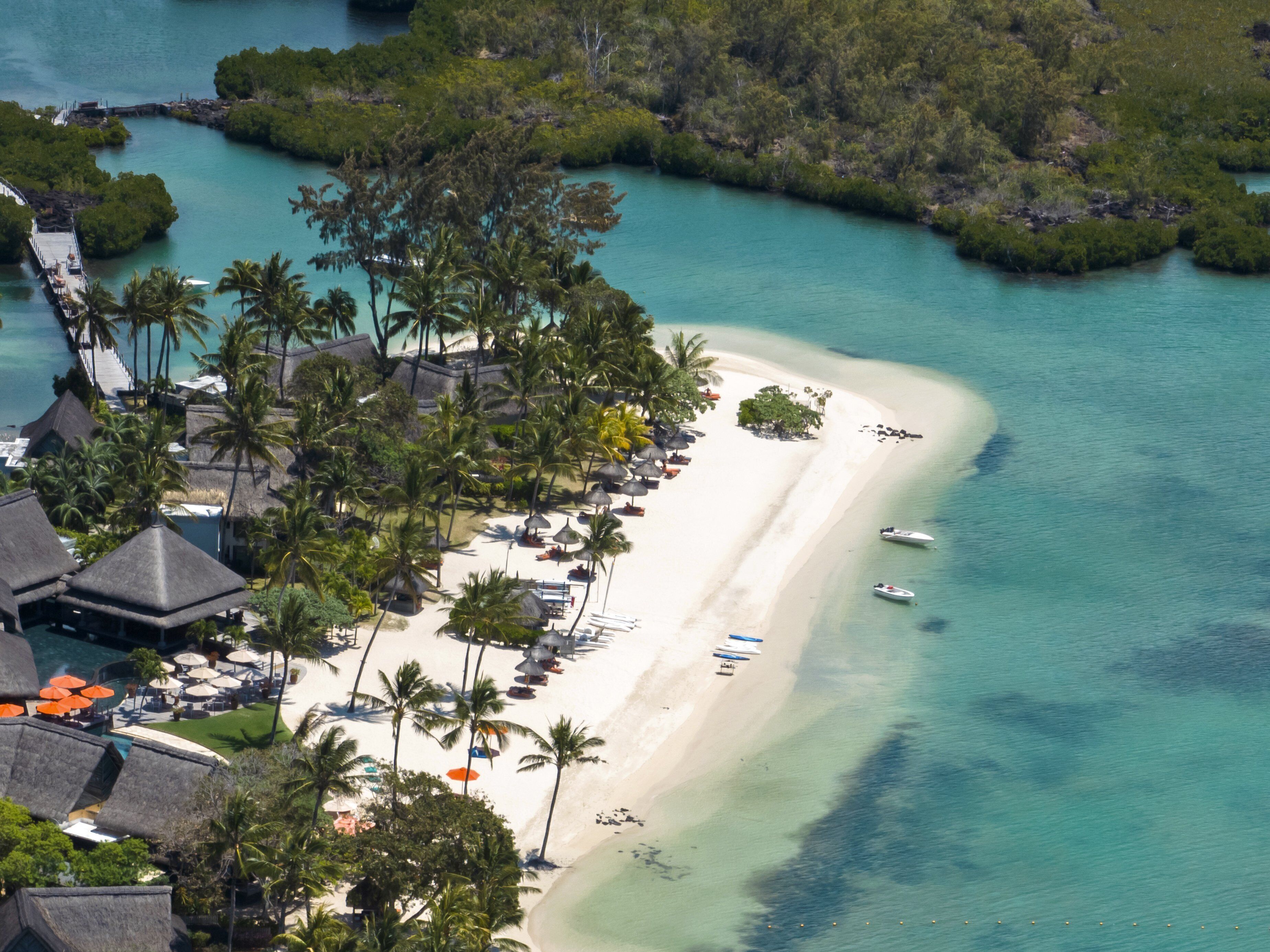 An aerial view of a tropical resort with a white sandy beach, palm trees, and thatched-roof buildings.