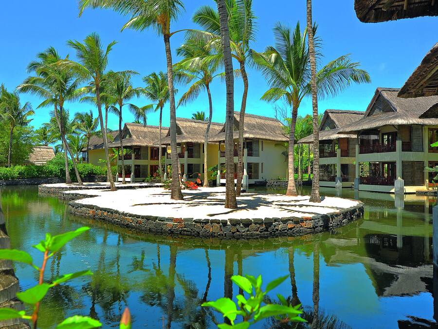 A resort with overwater bungalows, a clear pool, and palm trees.