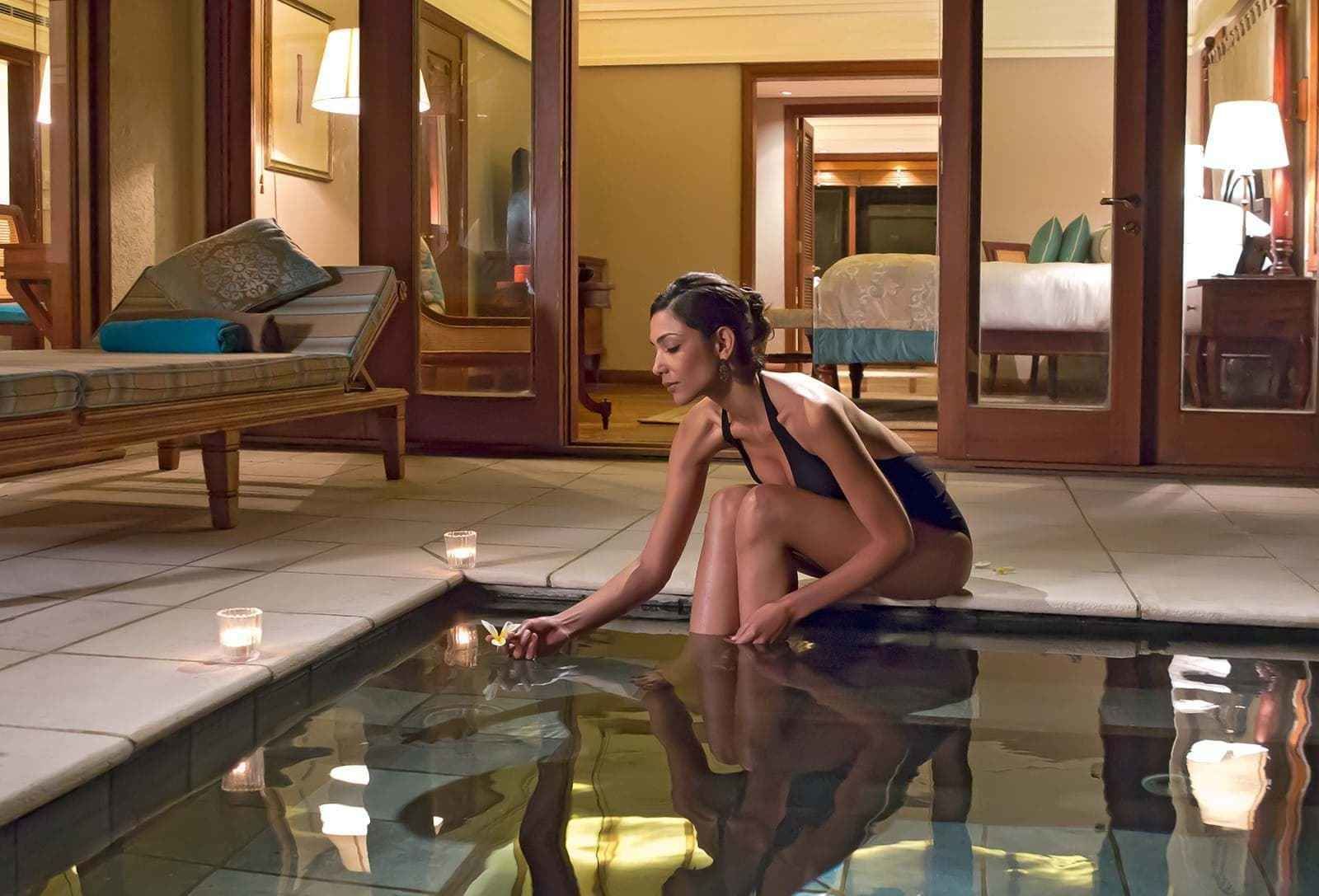 A person sitting by a reflective pool in a hotel room with a bed and a nightstand visible in the background.