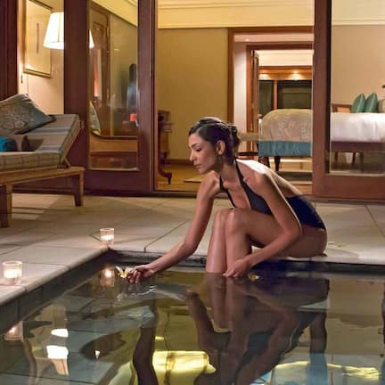A person sitting by a reflective pool in a hotel room with a bed and a nightstand visible in the background.