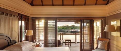 A hotel room with a large bed, a chair, a table, and a balcony with a view of the water.