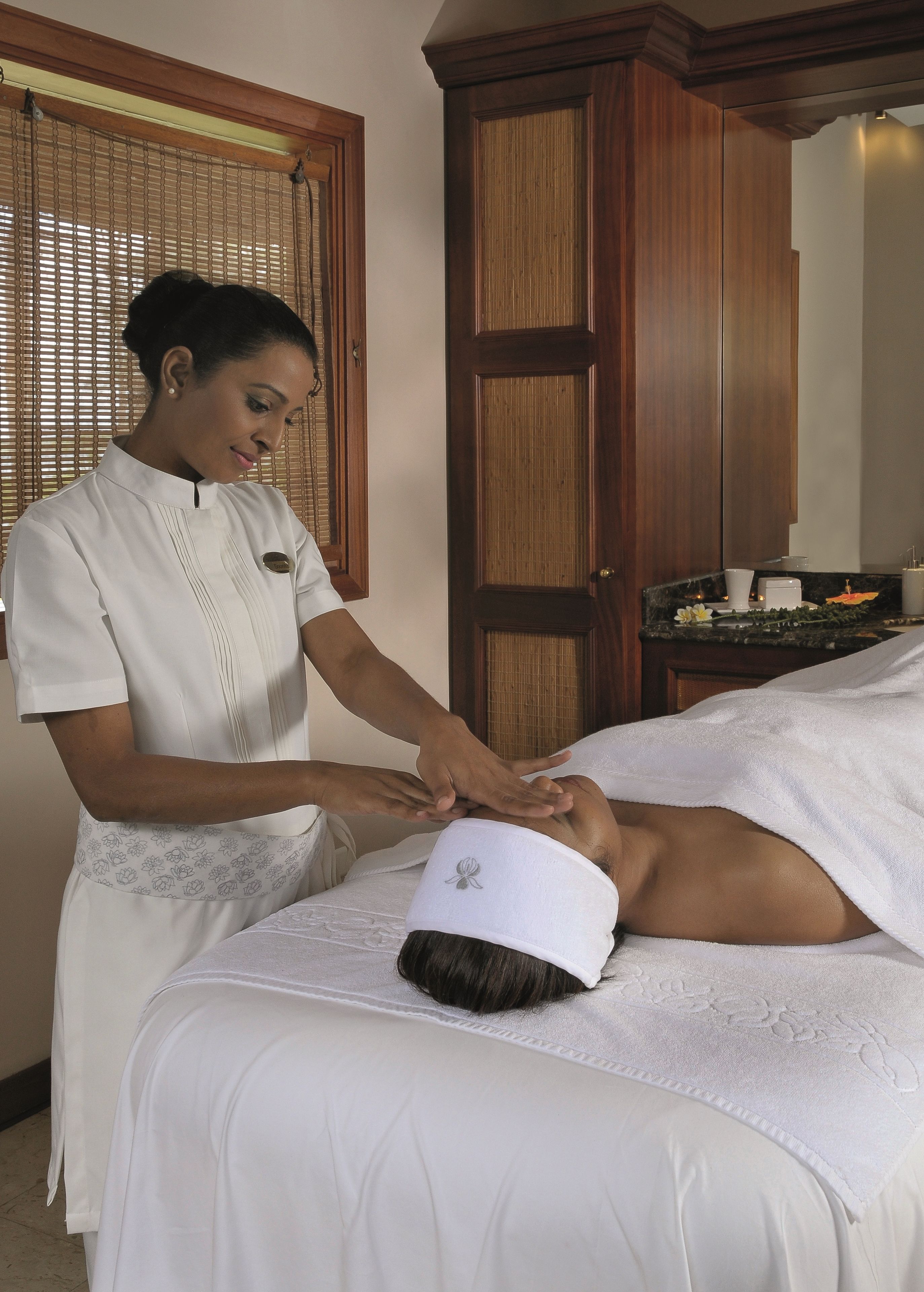 A massage therapy session in a room with a wooden door and blinds, a small table with a candle, and a white towel on the client.