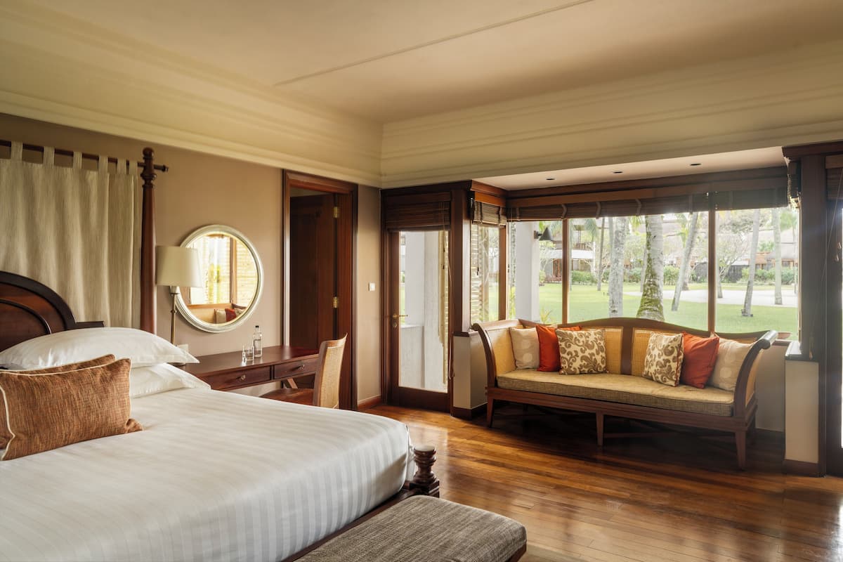 A hotel room with a large bed, a sitting area with a sofa, a mirror, and a view of a golf course.