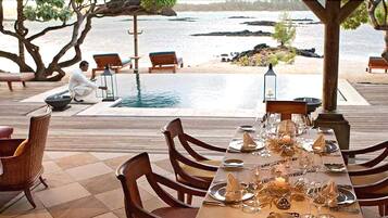 Un comedor con vista al mar, mobiliario de madera y una mesa dispuesta para una comida.