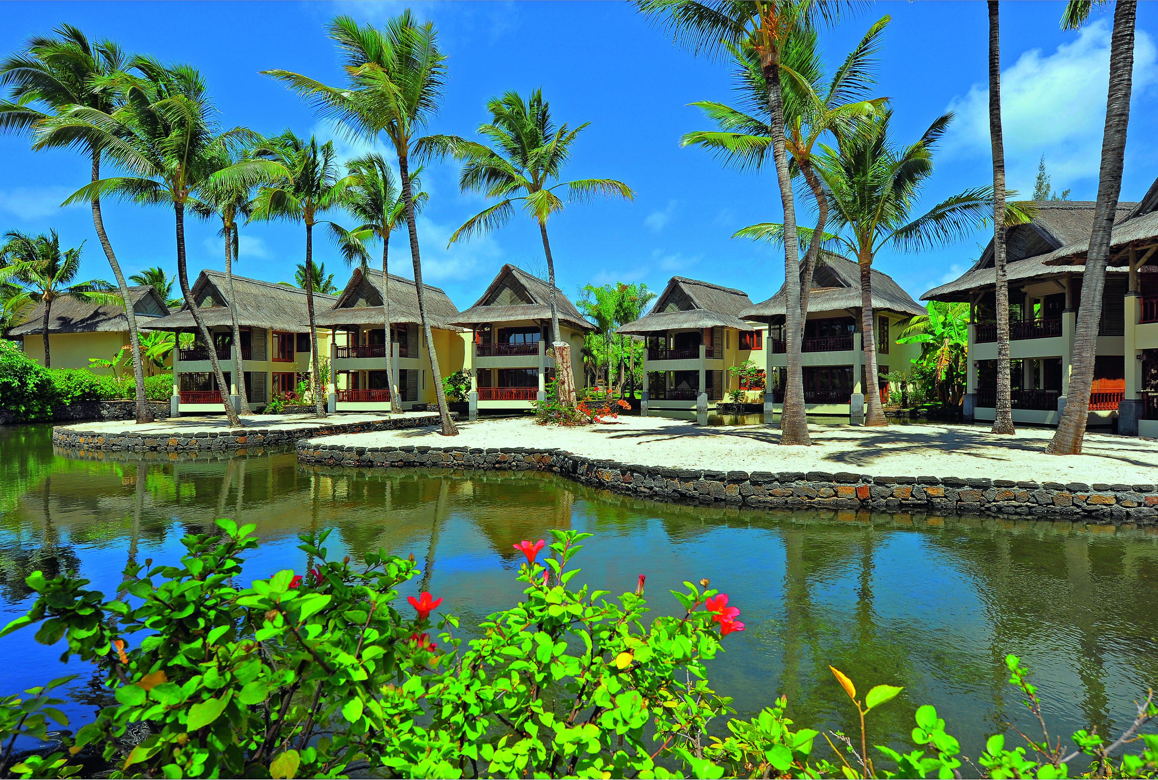 A resort with multiple bungalow-style buildings, a central water feature, and palm trees.