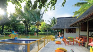 A pool area with a fenced pool, benches, and a thatched-roof building.