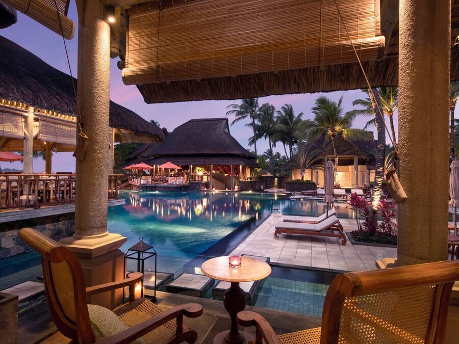 A resort pool area with lounge chairs, a table with a candle, and thatched-roof structures.
