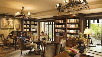 A spacious library with multiple bookshelves, comfortable seating, and a large chandelier.