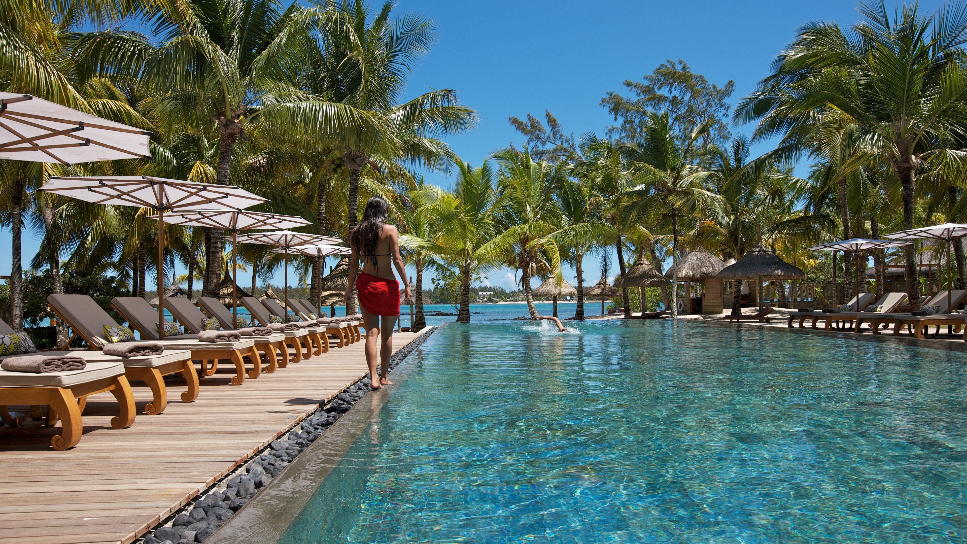 A poolside area with lounge chairs and umbrellas, surrounded by palm trees.