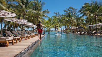 A poolside area with lounge chairs and umbrellas, surrounded by palm trees.