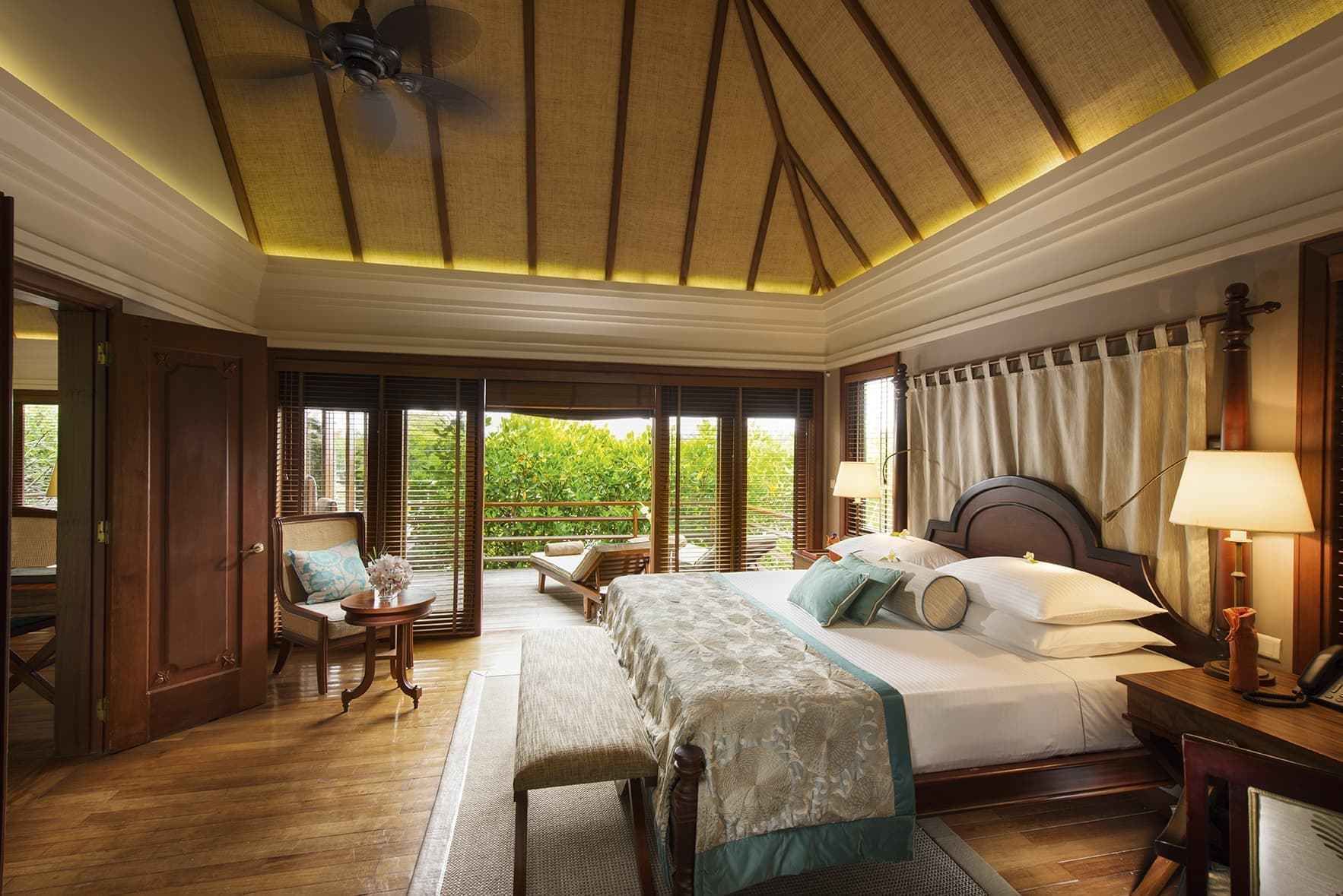 Een ruime slaapkamer met een groot bed, een zithoek met een stoel en tafel, en uitzicht op groen via de schuifdeuren.