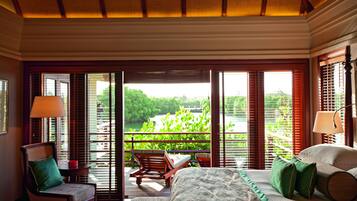A hotel room with a bed, a chair, a table, and a view of greenery and water outside.