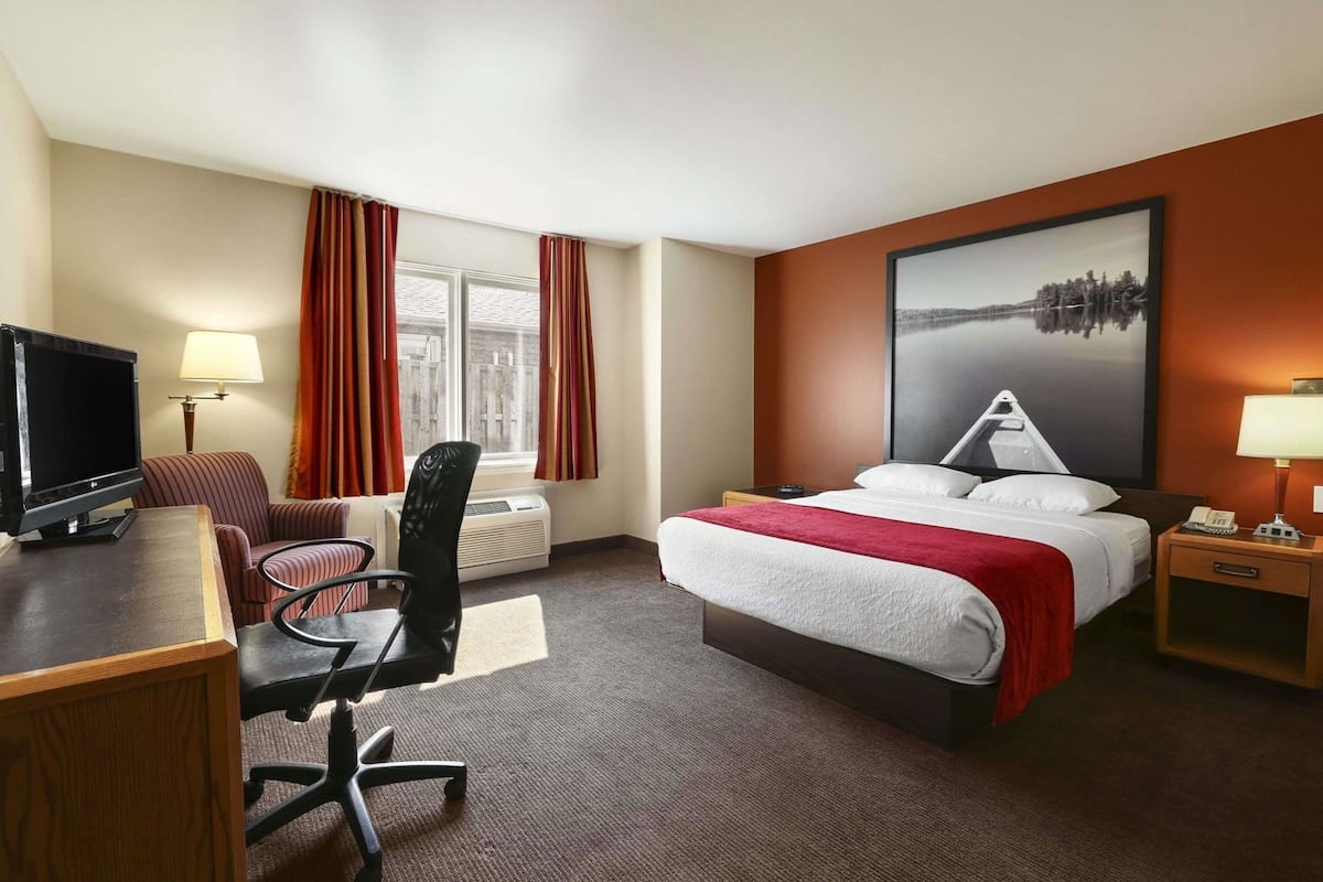 A hotel room with a bed, desk, chair, TV, and a painting on the wall.