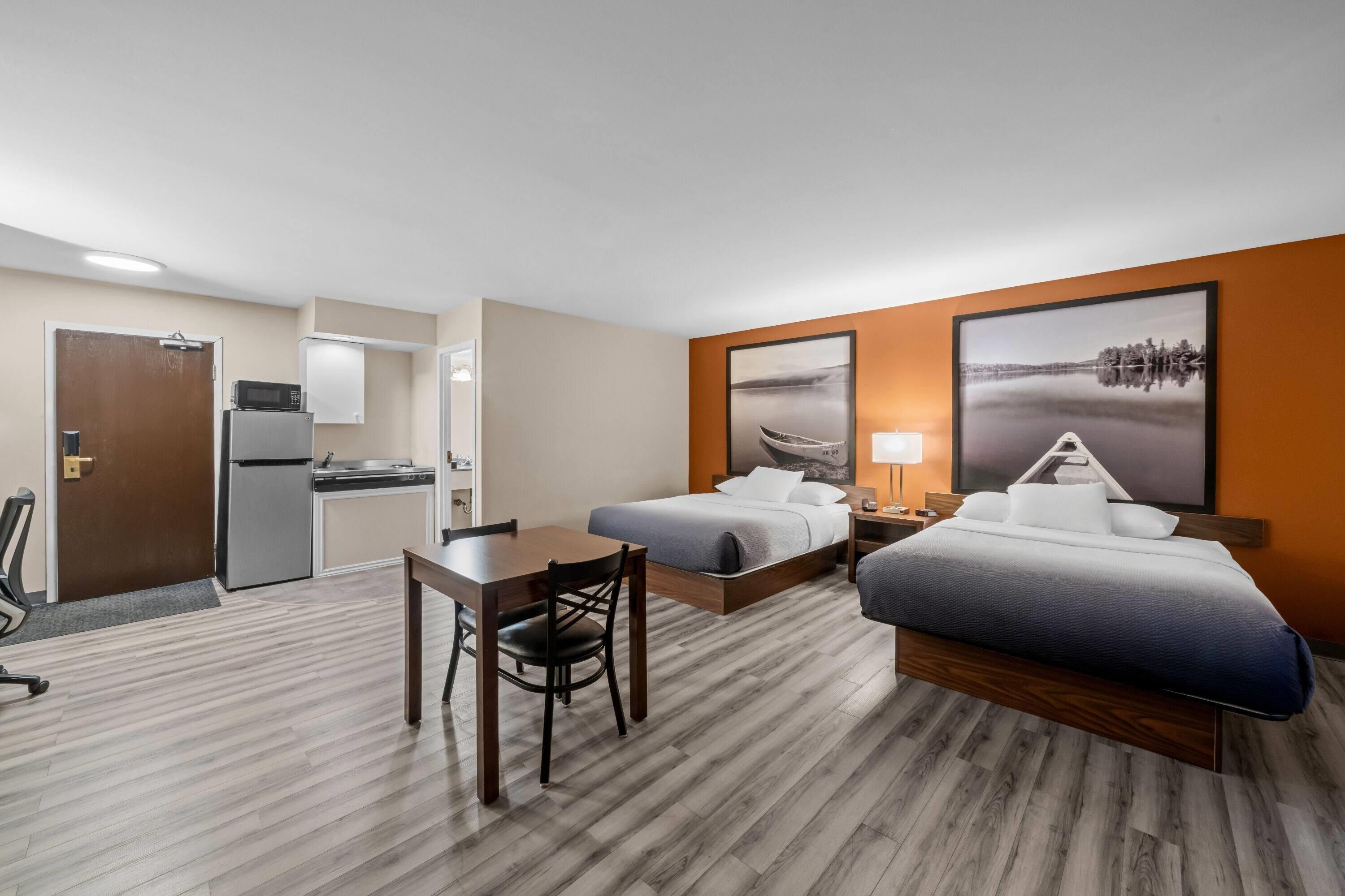 A hotel room with a kitchenette, two beds, a desk, and a chair.