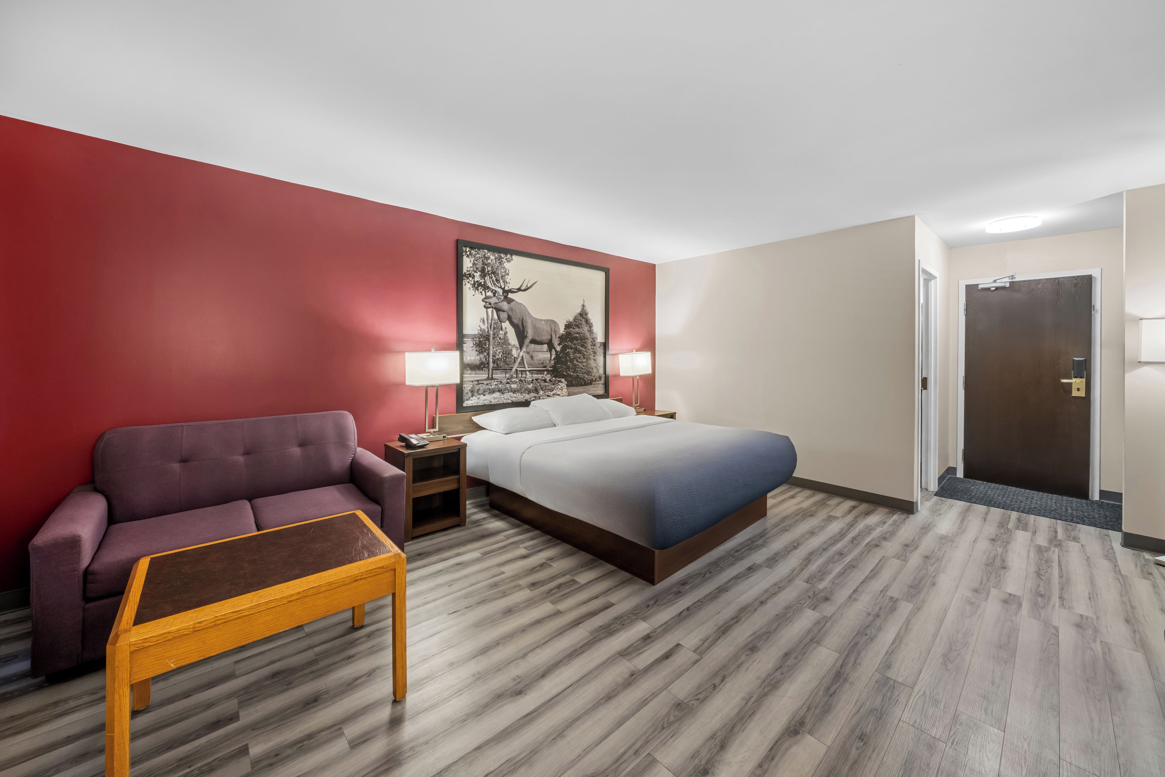 Una habitación de hotel con cama, mesita de noche, lámpara, sofá y una pequeña mesa.