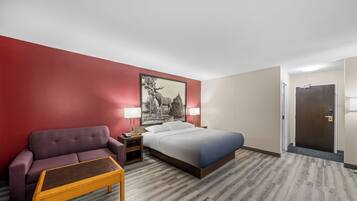 Una habitación de hotel con cama, mesita de noche, lámpara, sofá y una pequeña mesa.