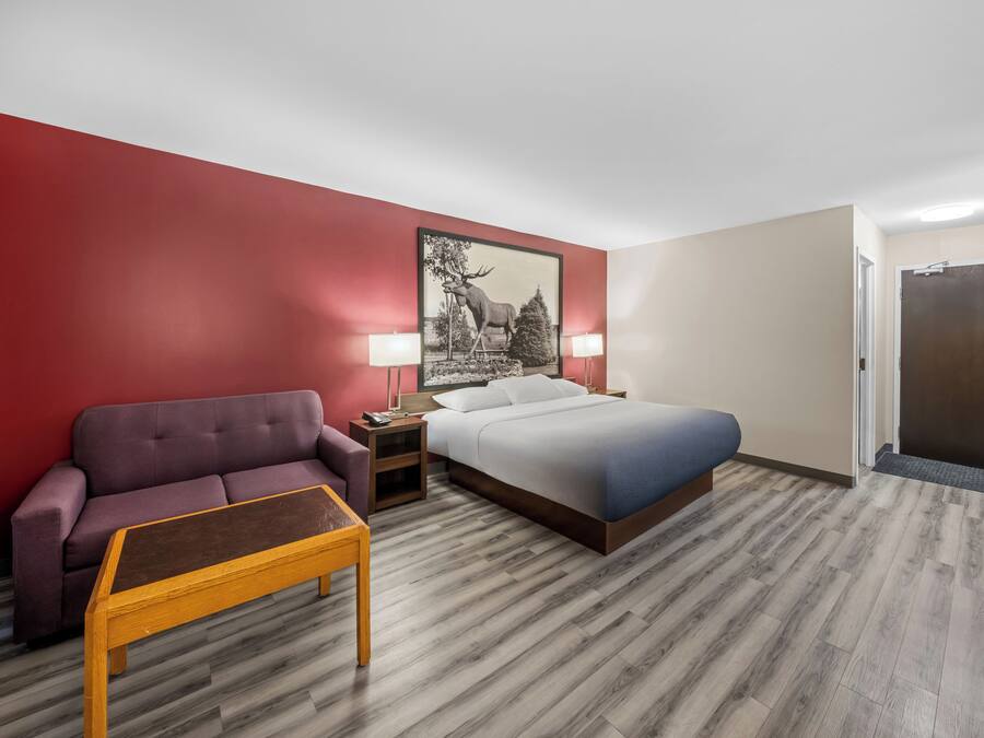 A hotel room with a bed, a nightstand, a lamp, a sofa, and a small table.