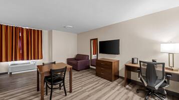 Una habitación de hotel con piso de madera, una mesa de comedor con sillas, un sofá, un televisor, un escritorio con una silla y una lámpara.