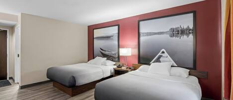 A hotel room with two beds, a nightstand, a lamp, and two large landscape paintings on the wall.
