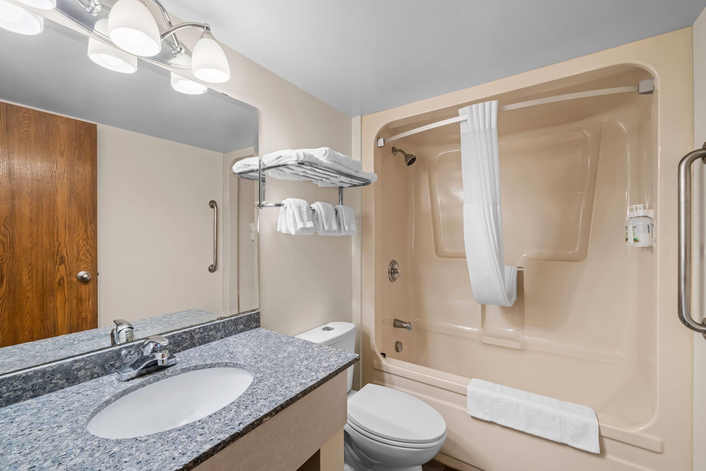 A bathroom with a sink, mirror, towel rack, and a bathtub with a showerhead.