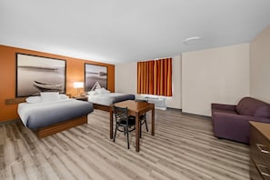 Habitación de hotel con cama, escritorio, silla, sofá morado y ventana con cortinas.