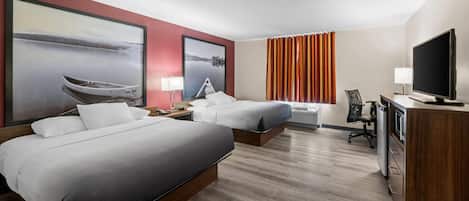 Habitación de hotel con dos camas, un escritorio con computadora, televisor y obras de arte en las paredes.