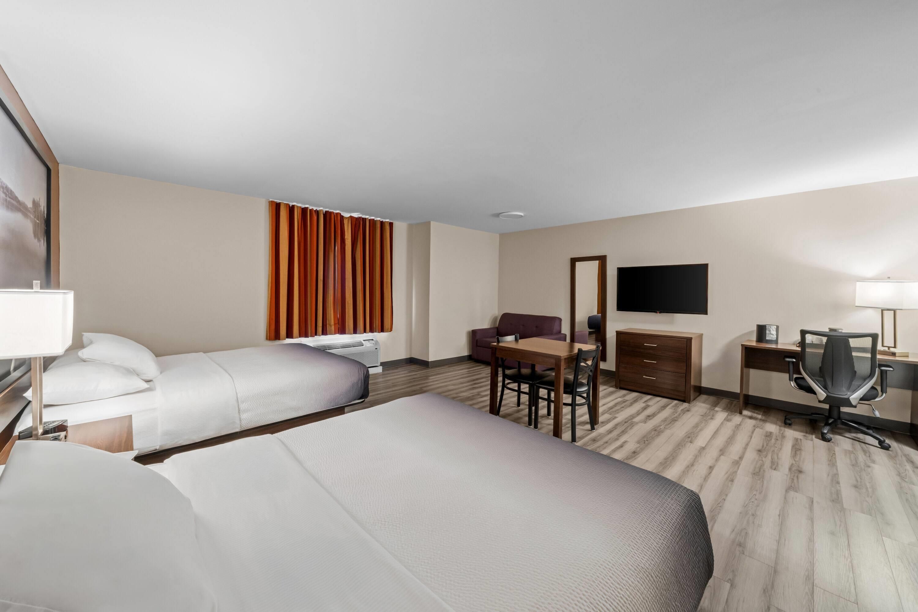 A hotel room with two beds, a desk, a chair, a sofa, a TV, and a mirror.