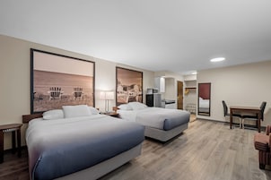 Habitación de hotel con dos camas, un escritorio, una silla y una pequeña kitchenette.