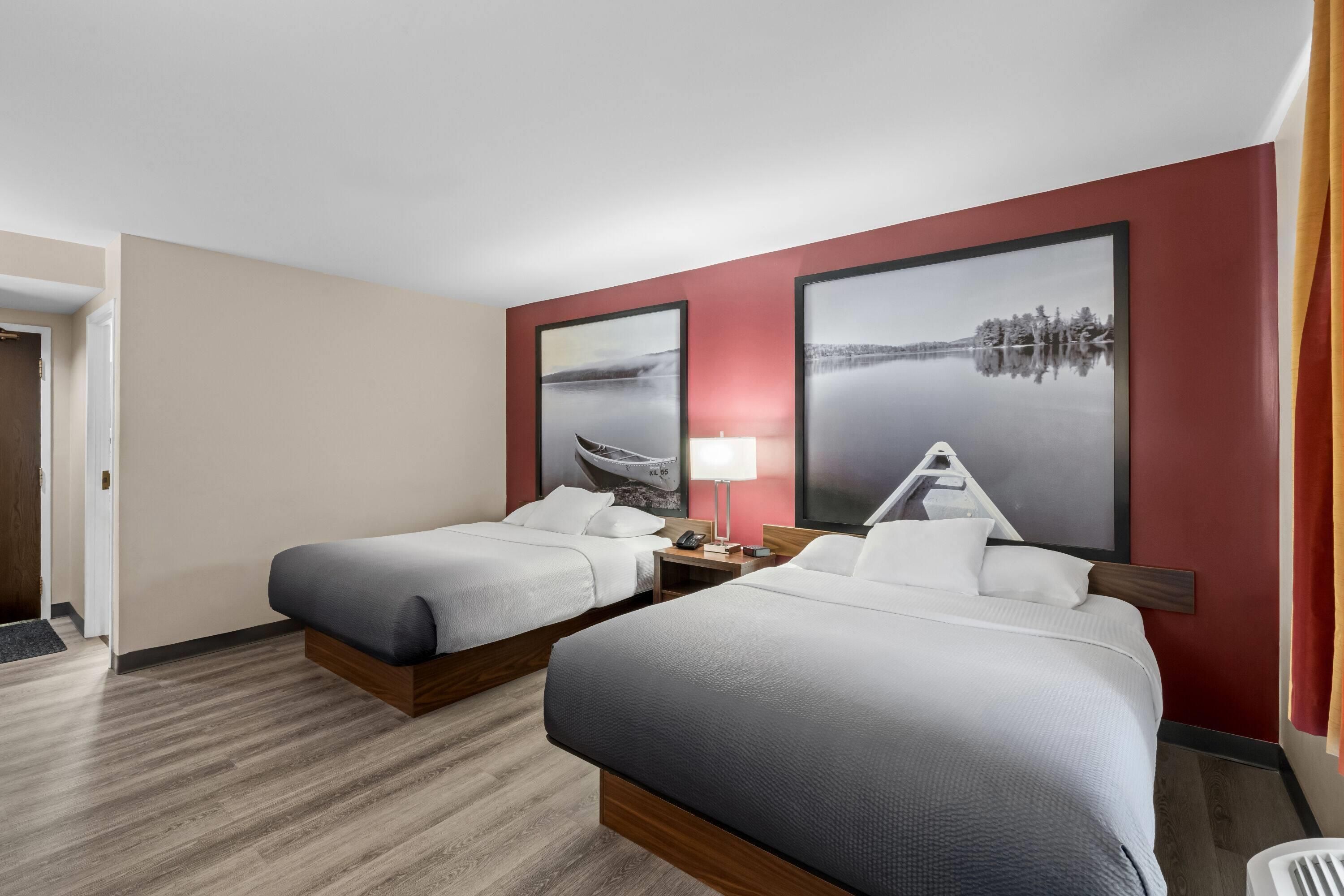Habitación de hotel con dos camas, una mesita de noche, una lámpara y dos grandes pinturas de paisajes en las paredes.