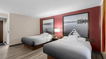 Habitación de hotel con dos camas, una mesita de noche, una lámpara y dos grandes pinturas de paisajes en las paredes.