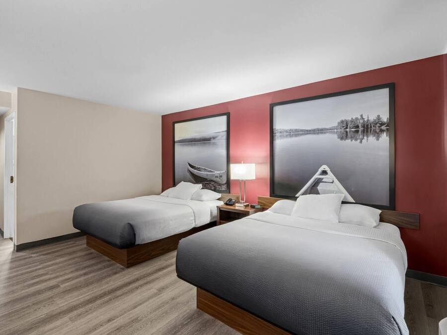 Camera d'albergo con due letti, un comodino, una lampada e due grandi dipinti di paesaggi alle pareti.
