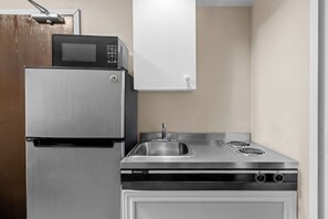 A compact kitchen with a stainless steel refrigerator, a microwave, and a stove with a sink. - Super 8 by Wyndham North Bay (North Bay)
