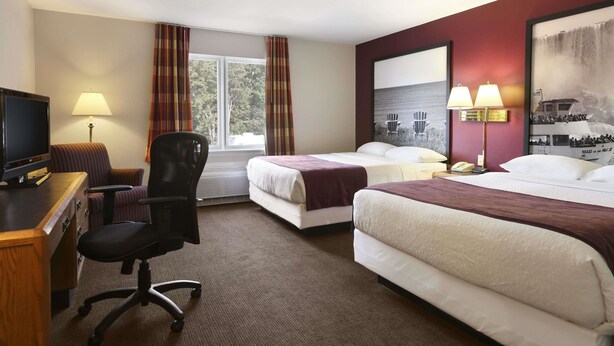 Habitación de hotel con dos camas, un escritorio con televisor, una silla y una ventana con cortinas.