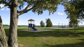 Un parque con un área de juegos, un árbol grande y vistas al agua.