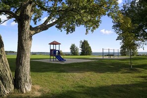 A park with a playground, a large tree, and a view of the water. - Super 8 by Wyndham North Bay (North Bay)